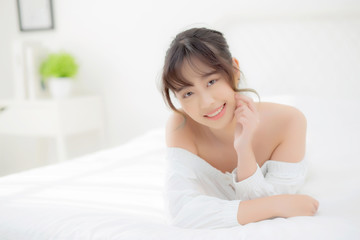 Obraz na płótnie Canvas Beautiful portrait young asian woman lying and smile while wake up with sunrise at morning, beauty cute girl happy and cheerful resting on bed in the bedroom, lifestyle and relax concept.