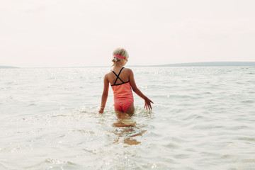 Little girl swimming in lake river with underwater goggles. Child diving in water on  beach. Authentic real lifestyle happy childhood. Summer fun outdoor aquatic activity. View from back.