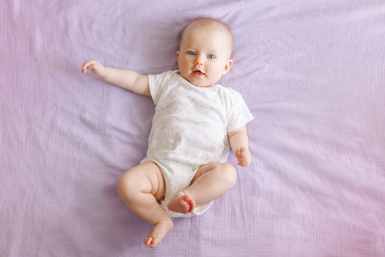 Portrait of cute adorable smiling white Caucasian baby girl boy with blue eyes four months old lying on bed looking at camera. View from top above. Happy childhood lifestyle.