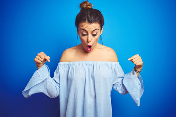 Young beautiful woman wearing bun hairstyle over blue isolated background Pointing down with fingers showing advertisement, surprised face and open mouth