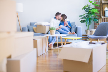 Fototapeta na wymiar Young beautiful couple sitting on the sofa kissing at new home around cardboard boxes
