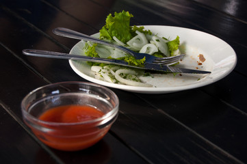leftover lettuce and onion rings on white plate with fork and knife next to red sauce bar