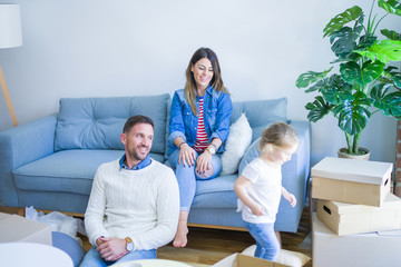 Beautiful family, parents sitting on the sofa drinking coffee looking his kid playing at new home around cardboard boxes