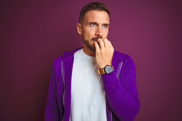 Young fitness man wearing casual sports sweatshirt over purple isolated background looking stressed and nervous with hands on mouth biting nails. Anxiety problem.