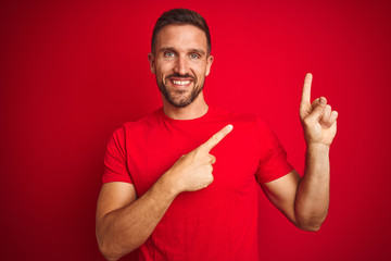 Young handsome man wearing casual t-shirt over red isolated background smiling and looking at the camera pointing with two hands and fingers to the side.