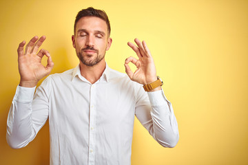 Young handsome man wearing elegant white shirt over yellow isolated background relax and smiling with eyes closed doing meditation gesture with fingers. Yoga concept.