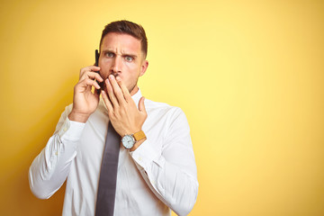 Young handsome business man talking on the phone over yellow isolated background cover mouth with hand shocked with shame for mistake, expression of fear, scared in silence, secret concept