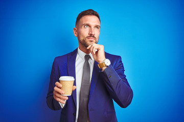 Young handsome business man drinking a coffee on a paper cup over blue isolated background serious...