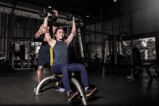 Young sport man and woman with dumbbells flexing muscles in gym.