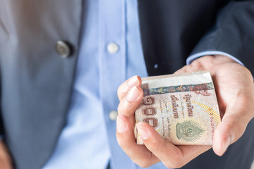 Businessman hand holding Thai Baht banknote stack. business, money, investment , finance and payment concepts
