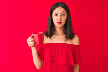 Young beautiful chinese woman drinking cup of coffee standing over isolated red background with a confident expression on smart face thinking serious