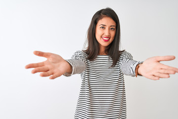 Young beautiful chinese woman wearing striped t-shirt standing over isolated white background looking at the camera smiling with open arms for hug. Cheerful expression embracing happiness.