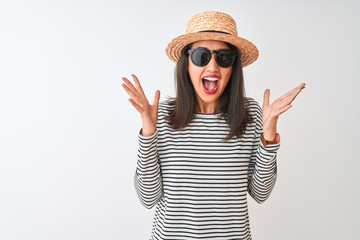 Chinese woman wearing striped t-shirt hat sunglasses standing over isolated white background celebrating crazy and amazed for success with arms raised and open eyes screaming excited. Winner concept