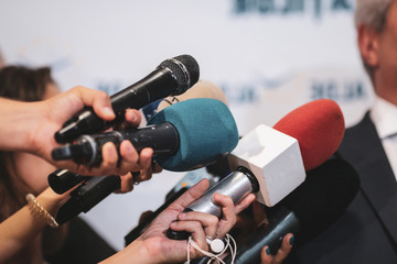 Details with the hands of journalists holding microphones in fron of a politician during a press conference - obrazy, fototapety, plakaty