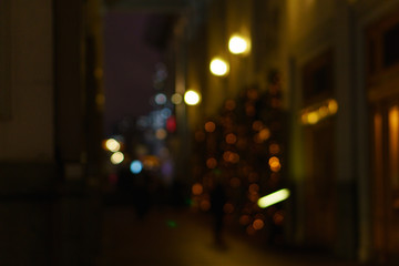 Defocused night city life people and street lamps. Bokeh urban city background effect. Holidays, sale and retail concept. Design background