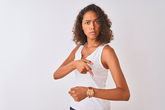 Young brazilian woman wearing casual t-shirt standing over isolated white background In hurry pointing to watch time, impatience, upset and angry for deadline delay