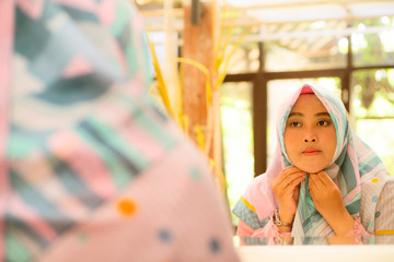 mirror reflection of young happy and beautiful Muslim woman in traditional hijab adjusting head scarf in beauty and fashion concept smiling in sweet face expression
