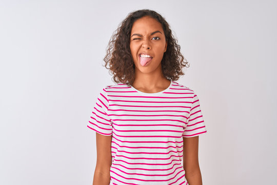 Young brazilian woman wearing pink striped t-shirt standing over isolated white background sticking tongue out happy with funny expression. Emotion concept.
