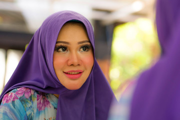 mirror reflection of young happy and beautiful Muslim woman in traditional hijab adjusting head scarf in beauty and fashion concept smiling in sweet face expression