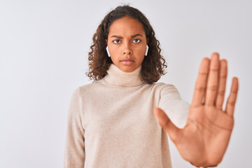 Brazilian woman listening to music using wireless earphones over isolated white background with open hand doing stop sign with serious and confident expression, defense gesture