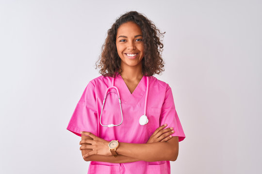 Young brazilian nurse woman wearing stethoscope standing over isolated white background happy face smiling with crossed arms looking at the camera. Positive person.