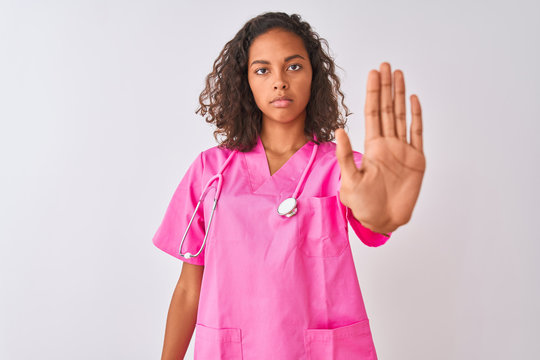Young brazilian nurse woman wearing stethoscope standing over isolated white background doing stop sing with palm of the hand. Warning expression with negative and serious gesture on the face.