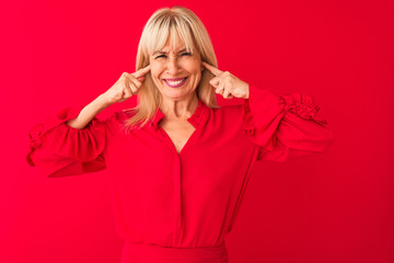 Middle age woman wearing elegant shirt standing over isolated red background covering ears with...