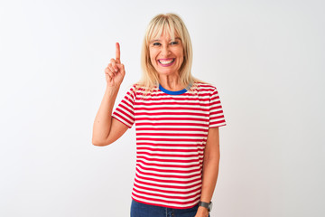 Middle age woman wearing casual striped t-shirt standing over isolated white background showing and pointing up with finger number one while smiling confident and happy.