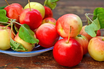 Red yellow apples with green foliage in blue saucer and scattered around it on old wooden plank surface. Close up