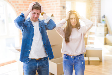 Beautiful young couple moving to a new house suffering from headache desperate and stressed because pain and migraine. Hands on head.