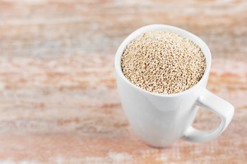 White cup filled with quinoa grains on wooden background