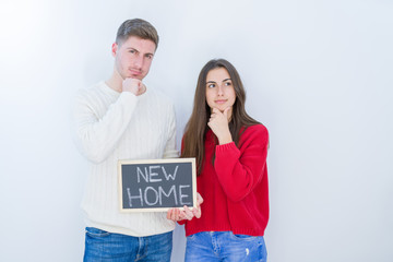 Beautiful young couple over white background holding blackboard with new home text serious face...