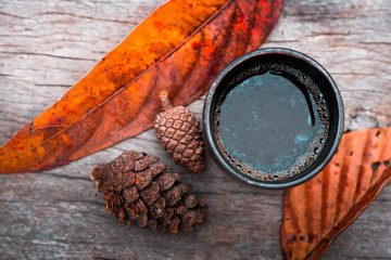 Cup of coffee on brown wooden table with pine cones and autumn leaves