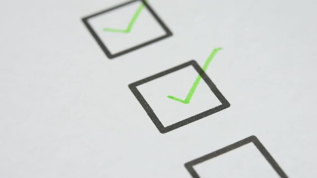green ink pen make a check mark sign in check box list on white paper. closed up and selective focus