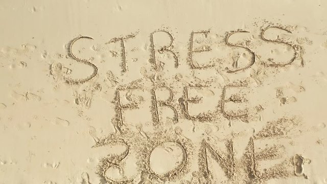 Shot with drone from the bottom to the top of the sand and the Caribbean ocean, written on the sand "Stress free zone", shot during the day, concept of vacation and fun.