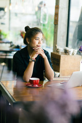Asian woman working in cafe and looking out window..