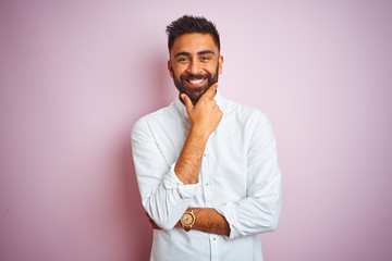 Young indian businessman wearing elegant shirt standing over isolated pink background looking confident at the camera with smile with crossed arms and hand raised on chin. Thinking positive.