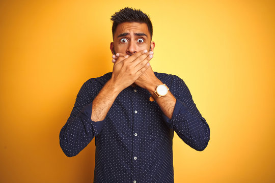 Young handsome indian businessman wearing shirt over isolated yellow background shocked covering mouth with hands for mistake. Secret concept.