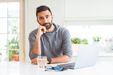 Fototapeta premium Handsome hispanic man working using computer laptop with hand on chin thinking about question, pensive expression. Smiling with thoughtful face. Doubt concept.