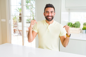 Handsome hispanic man casual yellow t-shirt at home looking confident with smile on face, pointing oneself with fingers proud and happy.