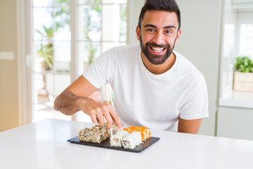 Handsome man smiling happy enjoying eating fresh colorful asian sushi using chopsticks