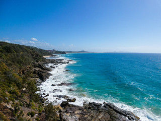 Fototapeta na wymiar Bright sunny summer beach day with vivid blue ocean in the background and cliffs in the foreground at Point Arkwright, Sunshine Coast, Queensland, Australia