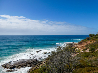 Fototapeta na wymiar Bright sunny summer beach day with vivid blue ocean in the background and cliffs in the foreground at Point Arkwright, Sunshine Coast, Queensland, Australia
