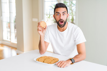 Handsome hispanic man eating healthy whole grain biscuits scared in shock with a surprise face, afraid and excited with fear expression