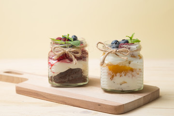 Raspberry cake in glass jar with fresh fruit and cream cheese on wooden background.
