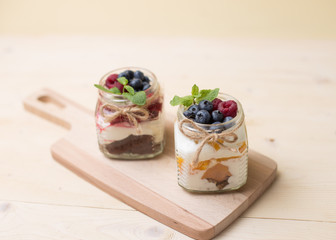 Raspberry cake in glass jar with fresh fruit and cream cheese on wooden background.