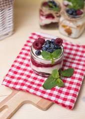 Raspberry cakes in glass jar with fresh fruit and cream cheese on a red napkin.