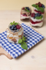 Raspberry cakes in glass jar with fresh fruit and cream cheese on a blue napkin.