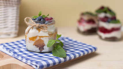 Raspberry cakes in glass jar with fresh fruit and cream cheese on a blue napkin.