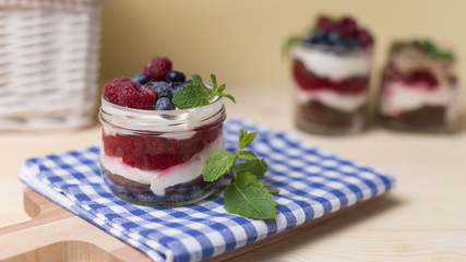 Raspberry cakes in glass jar with fresh fruit and cream cheese on a blue napkin.